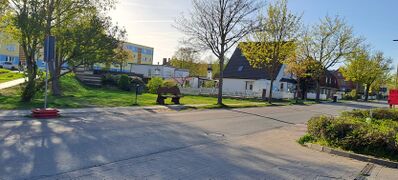 Gegenüber vom Netto auf der anderen Straßenseite eine Wiese mit Sitzbank