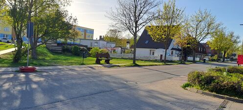 Gegenüber vom Netto auf der anderen Straßenseite eine Wiese mit Sitzbank